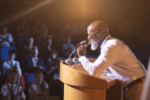old-businessman-standing-and-holding-speaker-to-sp-H2NKD8M(1)